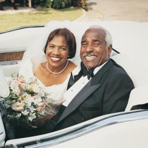 smiling senior couple marrying in later life, dressed in wedding outfits, sitting in open top car