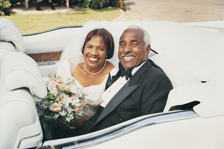 smiling senior couple marrying in later life, dressed in wedding outfits, sitting in open top car