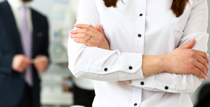 front of woman with crossed arms in business attire, with businessman in background. concept for disciplinary action