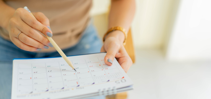 close up on hands, one holding a calendar and one marking off dates in pencil. concept for when people need additional support to remember dates for court hearings