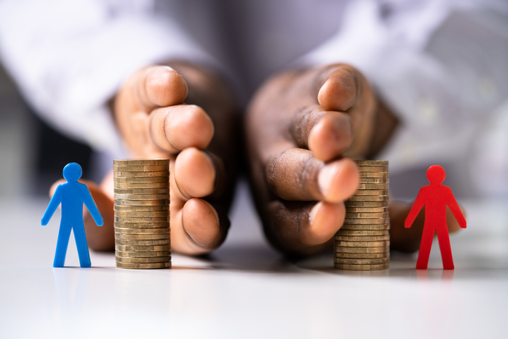 hands splitting coins with a paper cut out man in blue and red on either side, representing divorce finances