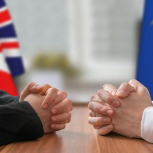 British flag and EU flag in background, with two men with folded hands on opposite sides of a table. Concept for how to enforce judgments of EU Courts in England