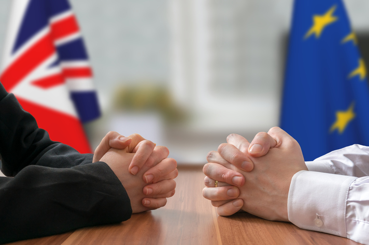 British flag and EU flag in background, with two men with folded hands on opposite sides of a table. Concept for how to enforce judgments of EU Courts in England