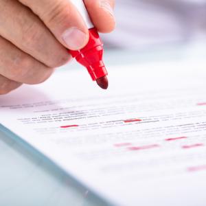 hand putting red pen to paper to edit words and amend a claim