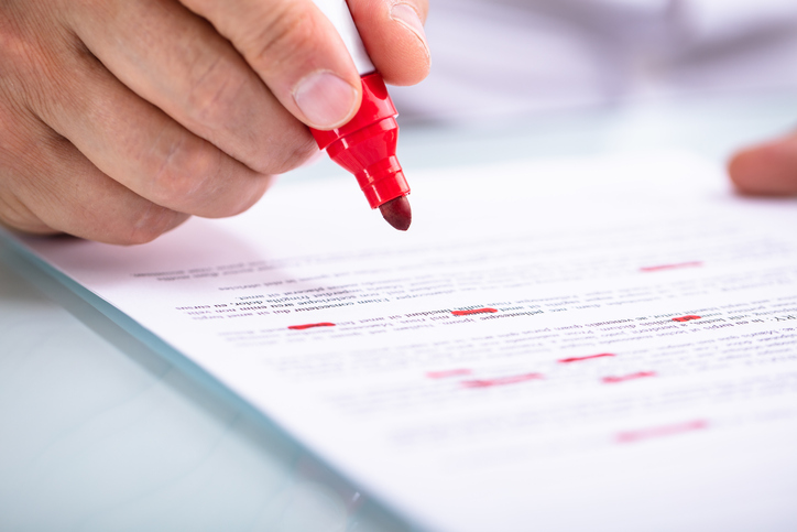 hand putting red pen to paper to edit words and amend a claim