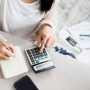 woman making notes and using calculator with paperwork behind her. concept for recovering debts