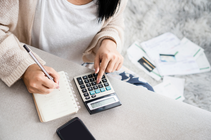 woman making notes and using calculator with paperwork behind her. concept for recovering debts