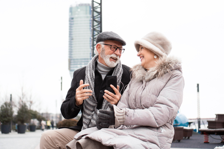 senior couple listening to music together on phone, smiling. concept for falling in love in later life