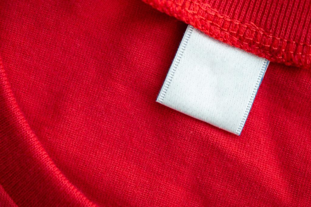 White blank clothing tag label on new red cotton shirt fabric texture background