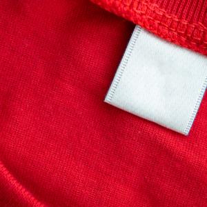 White blank clothing tag label on new red cotton shirt fabric texture background