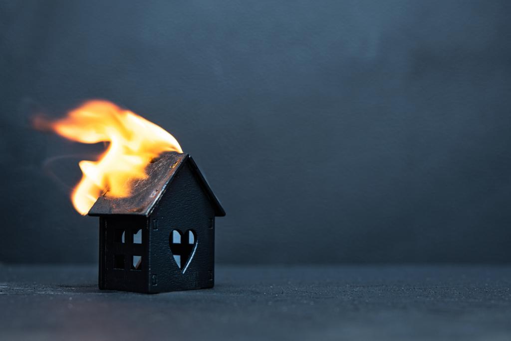 Black little wooden house caught fire on dark background. Concept of failure and compulsory home insurance.