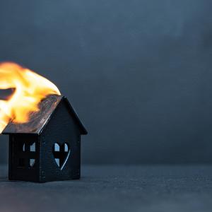 Black little wooden house caught fire on dark background. Concept of failure and compulsory home insurance.