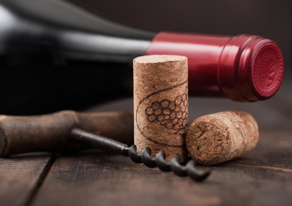 Wine corks with vintage corkscrew and bottle of red wine on wooden background.