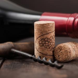 Wine corks with vintage corkscrew and bottle of red wine on wooden background.