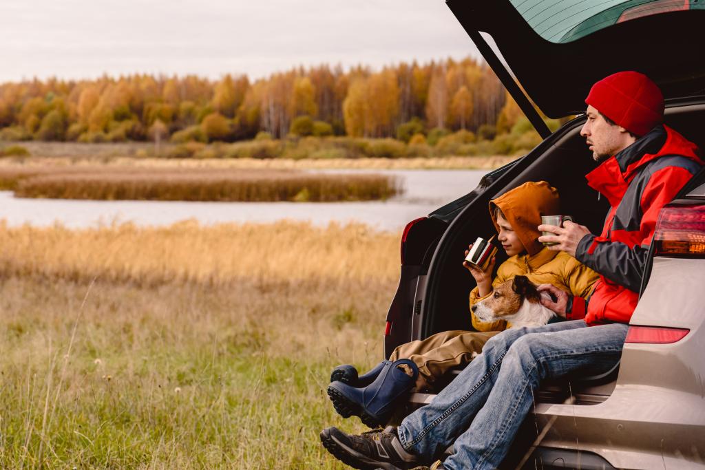 Father and son drinking tea sitting in car trunk