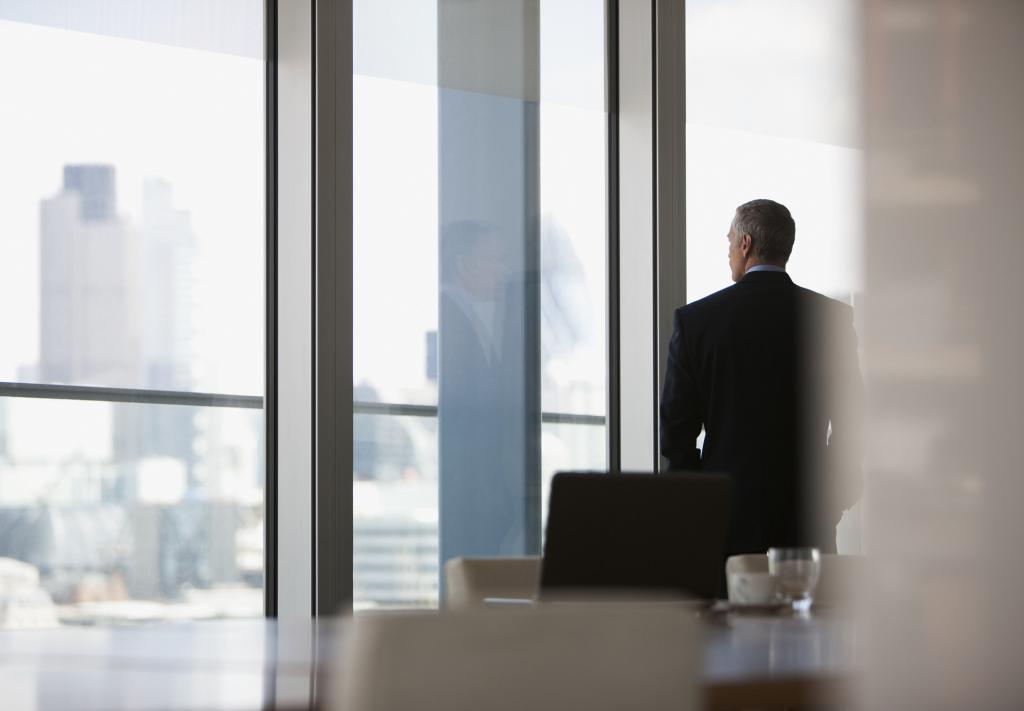 Businessman shown from behind looking out conference room window