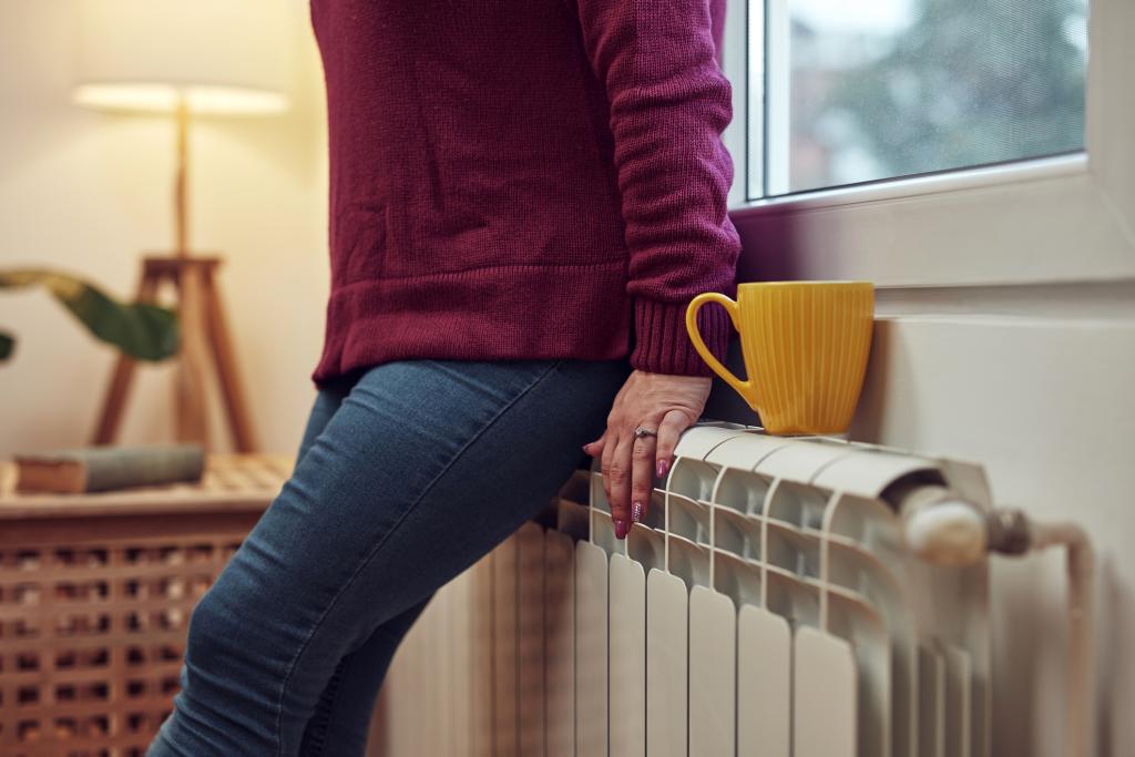 Woman heating up on a chilly winter day by leaning on a radiator