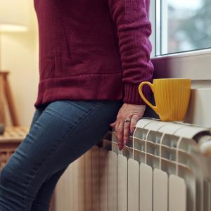 Woman heating up on a chilly winter day by leaning on a radiator