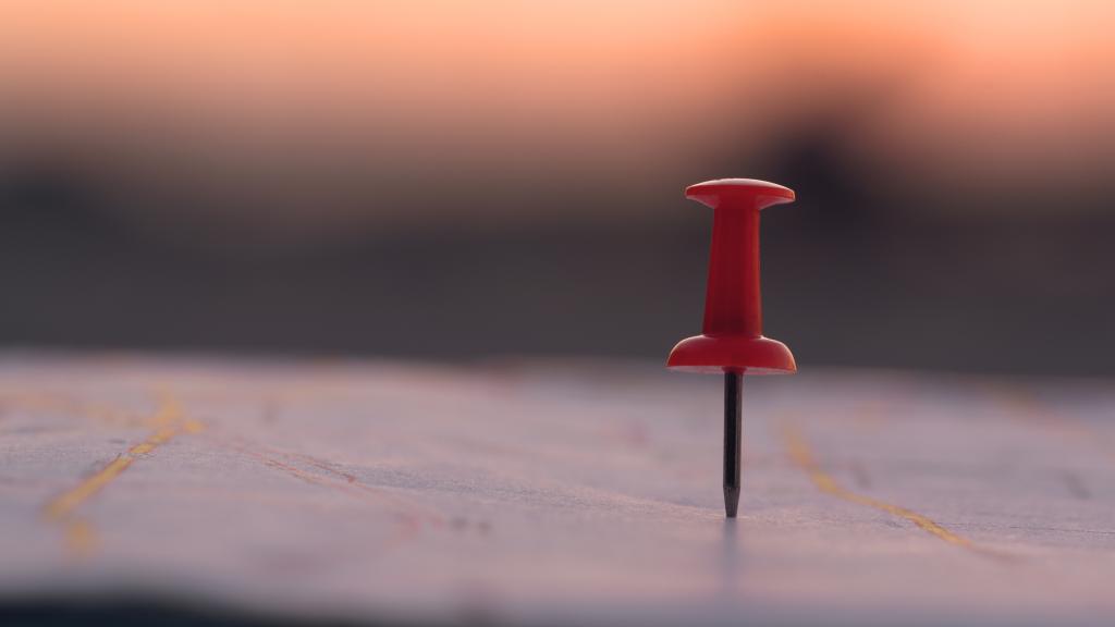 Close up red pin push map under sunset background.