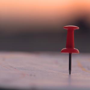 Close up red pin push map under sunset background.