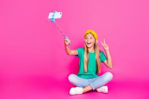 Photograph of a kidfluencer streaming on their phone in front of a pink wall