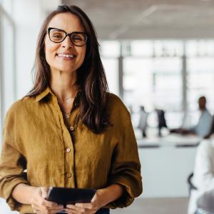 Business owner smiling at the camera in her office while employees work in background