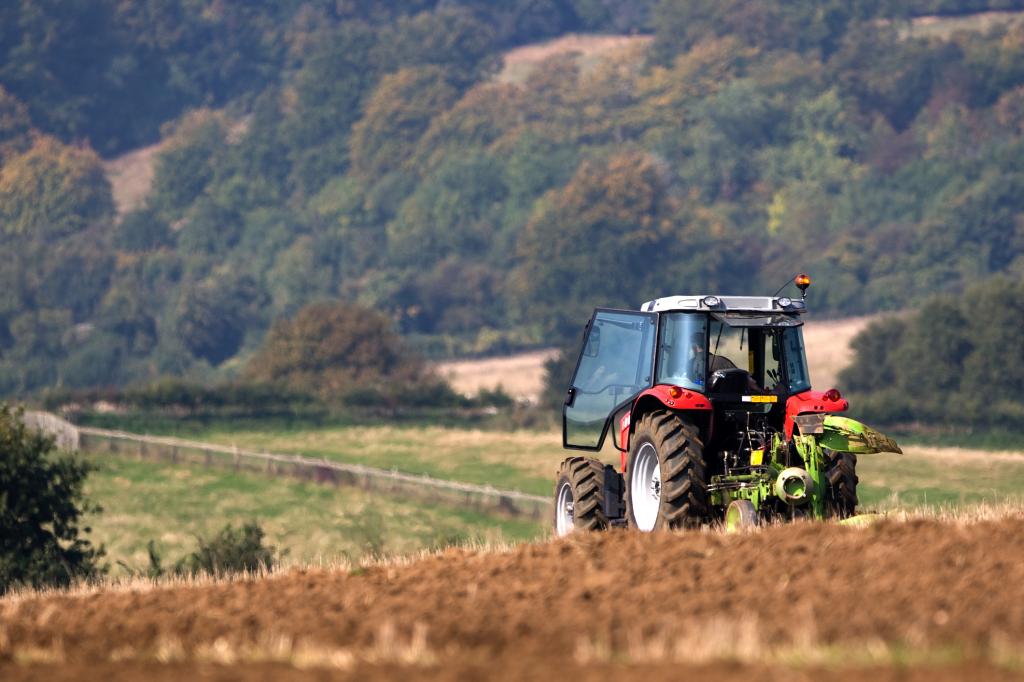 A red tractor ploughing a field in a rolling English landscape