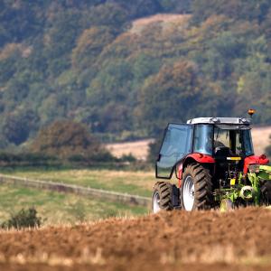A red tractor ploughing a field in a rolling English landscape