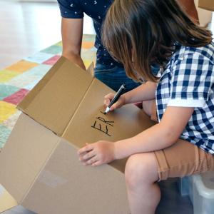 Little boy writing his name in a moving box with his father