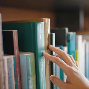 Close up hand search for book on bookshelves in the library.