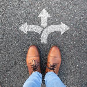 Business owner standing at a crossroads choosing employee ownership as a succession path.